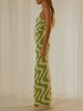 Side view of a model in Matcha Green Luxnometry Maxi Sweater Dress, showcasing the elegant silhouette and striking two-color pattern in a mansion hallway.