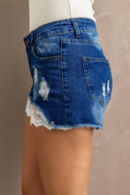 Model displaying the side view of Radiant Rise Lace-Trim Denim Shorts, showcasing the distressed detailing and soft lace hem. Ideal for summer vacations, brunch with friends, or running errands. Styled with a flowy off-shoulder blouse and sleek white sneakers for a breezy, chic look.