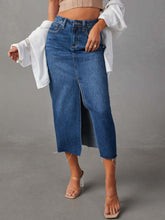 Front view of medium blue Denvara Raw Hem Front Slit Denim Midi Skirt styled with a dusty pink crop top layered with white button-down and clear heels