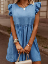 Model in medium blue Sylvenza Denim Dress styled with tan and gold handbag and accessories standing on urban city street.