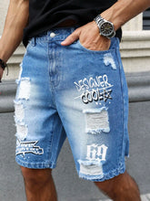Close-up side view of men's blue ripped text logo printed denim shorts on model.