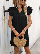 Model wearing the black ruffled notched cap sleeve mini dress with a straw handbag.