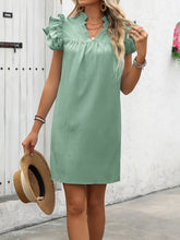 Model posing with a hat and round straw earrings  wearing the Calivémuse™ sage dress.