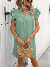 Model wearing the sage ruffled notched cap sleeve mini dress paired with a woven brown handbag, straw hat, jewelry, and sunglasses.
