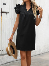 Model posing with a straw hat wearing the black ruffled notched cap sleeve mini dress.