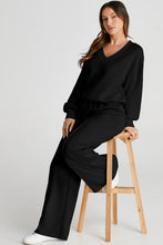 Model seated on bar stool in Black MotoLux VesperActive set, legs crossed casually.
