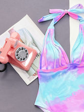 Close-up flat lay detail of multicolor tie-dye one-piece swimsuit showing upper 3D line texture and halter neck design