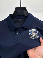 Close-up front view of navy blue Equestrian Crest Designer Polo on hanger showing embroidery, buttons, and flip color-contrast collar.