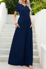Model with hands in pockets, styled in navy blue Blissurella Maxi Tee Dress with layered gold jewelry and tan heels for a casual café outing.