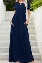 Model posing on a white staircase wearing the navy blue Blissurella Maxi Tee Dress styled with statement jewelry and tan heels for a seaside getaway.