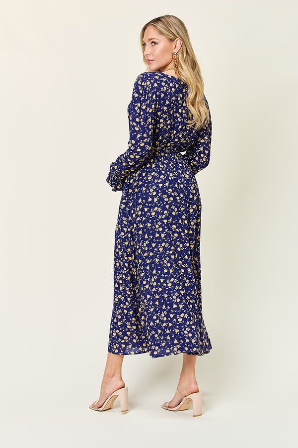 Model back view of  navy Flounce & Tie Midi  dress paired with jewelry and clear tan heels with white background.