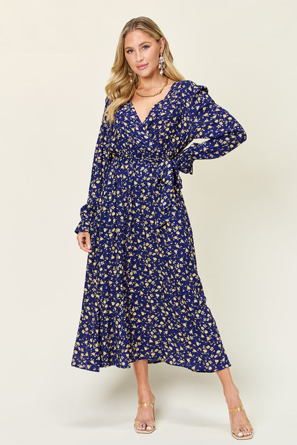 Model posing in a Navy color Flounce & Tie Midi dress paired with jewelry and clear gold heels.