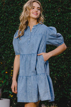 Woman strolling through an outdoor café district with hand in pocket wearing ODDI Washed Tiered Mini Denim Dress paired with gold hoops and nude sandals.