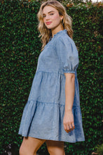Side view of model wearing ODDI Washed Tiered Mini Denim Dress highlighting relaxed fit, pockets, and soft flowy tiers with a topiary bush background.