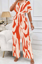 Model in Orange Oléavia Luxe Jumpsuit walking along a palm-lined boardwalk at golden hour.