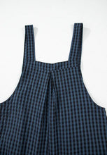 Close-up flatlay of the top back half of dark blue plaid overalls highlighting the center pleat, wide straps, and soft woven fabric texture.