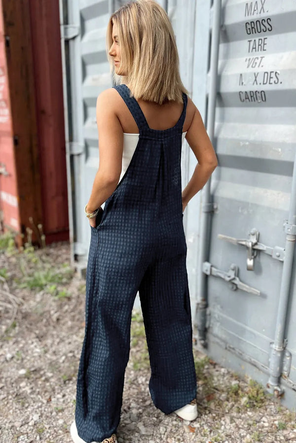 Model showing back view of wide strap plaid overalls, relaxed fit and adjustable button straps.