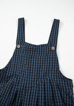 Close-up of front button and chest pocket on dark blue plaid overalls.