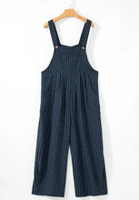 Dark blue plaid wide-leg overalls front view hanging on a wooden hanger.