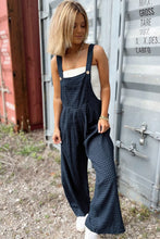 Lifestyle shot of model lounging on a picnic blanket in plaid overalls, sipping iced tea.