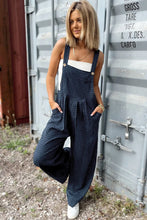 Side profile of model in wide-leg dark blue plaid overalls with visible side pocket detail.