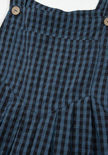Flatlay of the top half of plaid overalls showing chest pocket and straps.