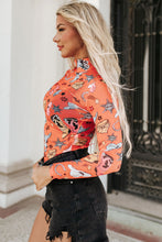 Side profile of model in an orange Printed Mock Neck Long Sleeve Bodysuit, showcasing the sleek fit and mock neckline, styled with high-waisted black pants.