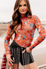 Lifestyle image of model in an orange Printed Mock Neck Long Sleeve Bodysuit, laughing with friends at a rooftop hangout, styled with black trousers and bold earrings.