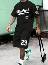 Man wearing a onyx Orrik 3D Printed Motion Set with 'New York Brooklyn 23' text on red round neck tee and onyx shorts with '23' on them. 