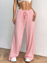 Female model in Blush Pink Orvella LumaTide Striped Wide Leg Pants styled with a white short-sleeved blouse, jewelry, and white sneakers.