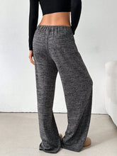 Back view of female model in Dark Grey Orvella LumaTide Striped Wide Leg Pants, paired with a black long-sleeved blouse, jewelry, black purse, and light brown boots.