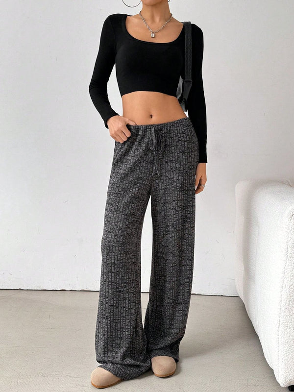 Female model wearing Dark Grey Orvella LumaTide Striped Wide Leg Pants, styled with a black long-sleeved blouse, layered jewelry, a black purse, and casual light brown boots, front view.