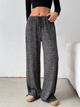 Relaxed lifestyle shot of a female model wearing Dark Grey Orvella LumaTide Striped Wide Leg Pants styled with a black blouse, accessories, and light brown boots.