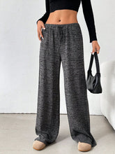 Side view of female model wearing Dark Grey Orvella LumaTide Striped Wide Leg Pants, black blouse, jewelry, and light brown boots.