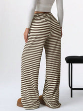 Back view of Taupe Orvella LumaTide Striped Wide Leg Pants paired with a white long-sleeved blouse, jewelry, and brown boots.