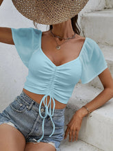 Woman wearing Glowflutter Crop Top with sheer flutter sleeves and front drawstring in pastel blue, styled with denim jeans.