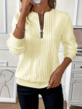a woman modeling the pastel yellow Sunset Coastal Bliss Texture Half Zip Long Sleeve Sweatshirt paired with jewelry, and dark blue denim jeans while taking a selfie photo at the studio