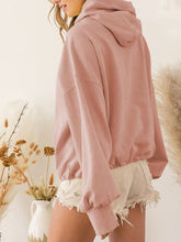 A model showcasing the back of a peach color Nuvella Zip-Up Dropped Shoulder Hoodie paired with distressed tan denim shorts.