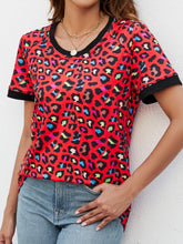 Model wearing a red leopard print round neck tee, laughing with friends at a rooftop café, styled with cutoff denim shorts and statement sunglasses.
