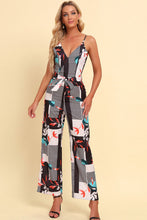 Model wearing the Rexéa white floral jumpsuit with spaghetti straps and a waist tie, standing in a sunlit garden.