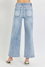 A female posing from the back wearing light blue RISEN Full Size Tummy Control High Rise Crop Wide Leg Jeans paired with a floral white blouse, jewelry, and white round open-toe heels.
