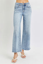 A female posing from the side wearing light blue RISEN Full Size Tummy Control High Rise Crop Wide Leg Jeans paired with a floral white blouse, jewelry, and white round open-toe heels.