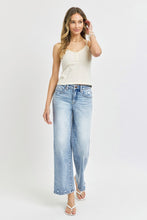 A female posing from the front wearing light blue RISEN Full Size Tummy Control High Rise Crop Wide Leg Jeans paired with a floral white blouse, jewelry, and white round open-toe heels.