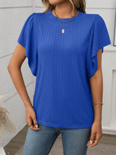 Model in a royal blue Round Neck Flutter Sleeve T-Shirt, styled with wide-leg linen pants and a straw tote at a sunny garden brunch.