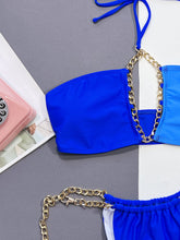 Close-up flat lay detail of royal blue chain detail halter neck bikini set showing chain accents and contrast pattern fabric