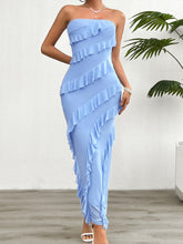 Model in the Light Blue Seraflore™ Maxi Dress standing beside a tropical plant in a resort garden.