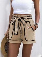Side view of model holding straw hat while wearing Seravelya Wave Shorts in tan