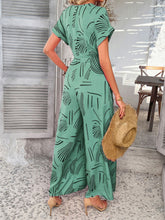 Model back view in gum leaf Serenoor jumpsuit, styled with suede tan open-toe heels, and straw hat at a beach house.