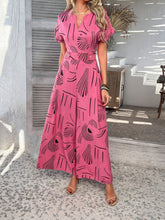 Front view of Serenoor jumpsuit in hot pink with elegant silhouette, styled with tan open-toe heels, jewelry, and woven clutch at a beach house.