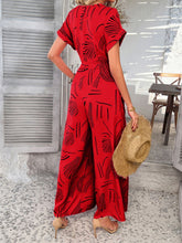Model back view in scarlet Serenoor jumpsuit, accessorized with tan heels and clutch at a beach house.